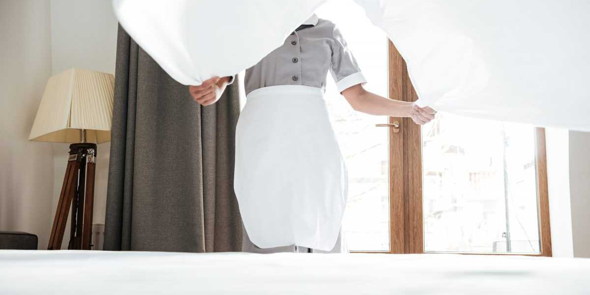 A maid in a white apron holding a sheet over a bed.