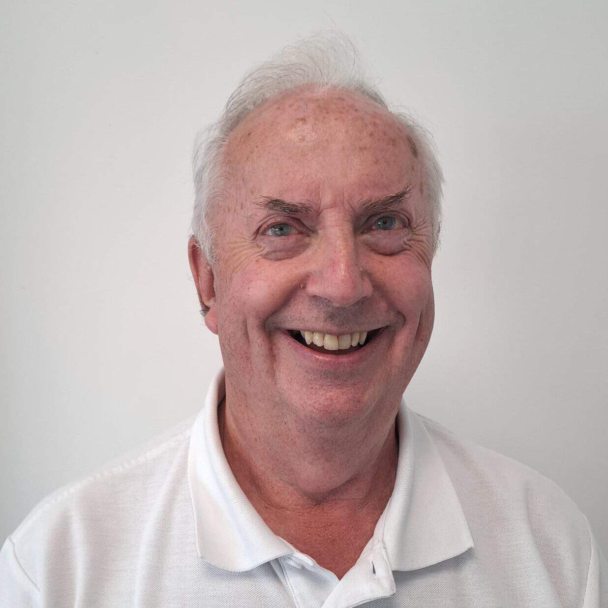 An older man smiling in a white polo shirt.