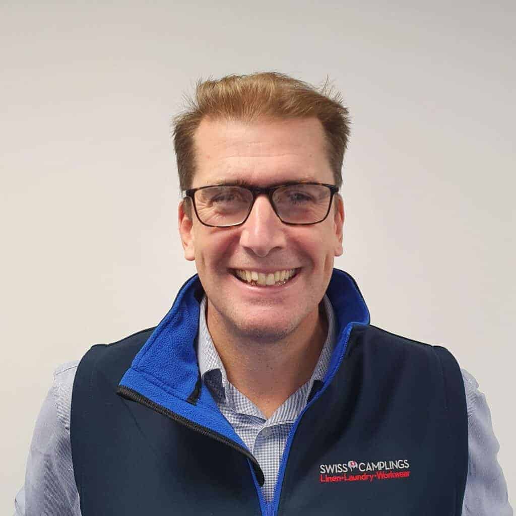 A man wearing glasses and a blue vest is smiling.