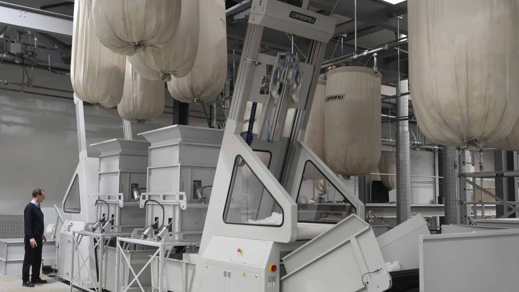A man is standing in a room surrounded by a multitude of bags, including Swiss Camplings.