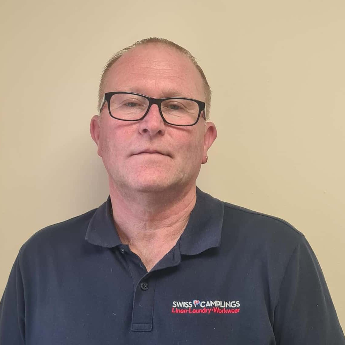 A man wearing glasses and a blue shirt standing in front of a wall.