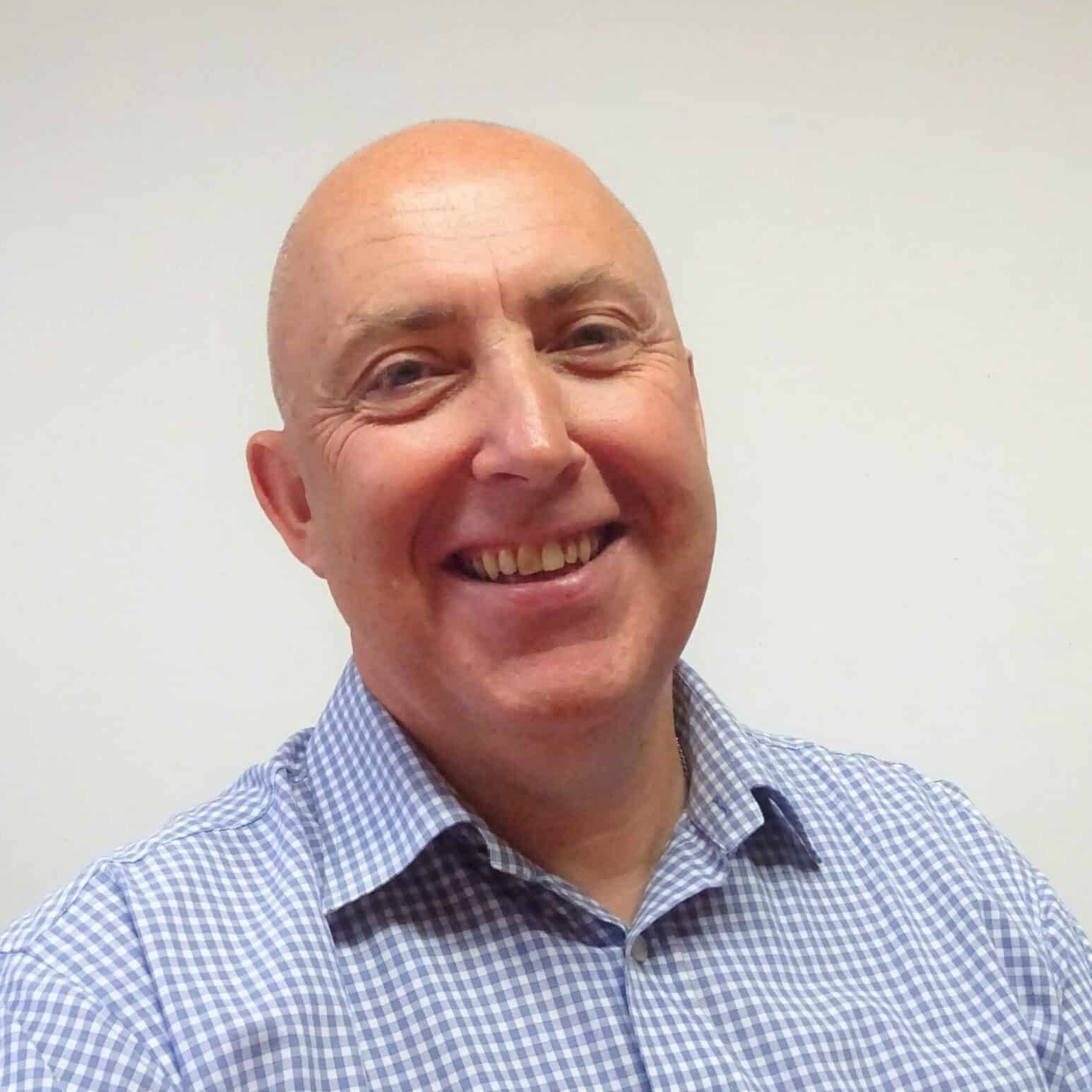A bald man smiling in front of a white wall.