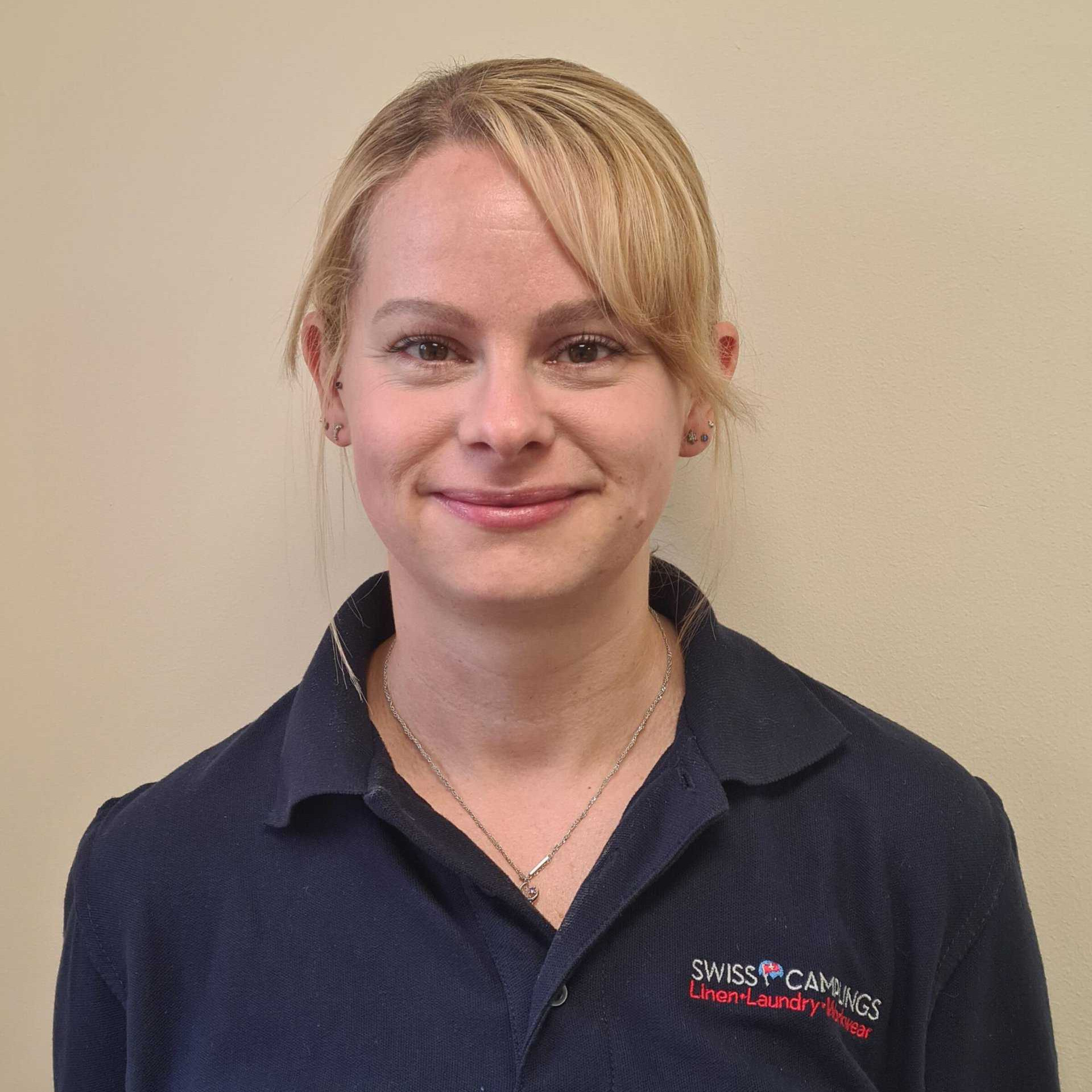 A woman in a blue polo shirt standing in front of a wall.