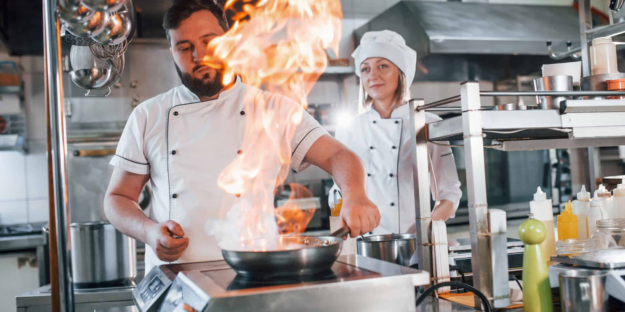 Flames in the frying pan. Professional chef preparing food in the kitchen