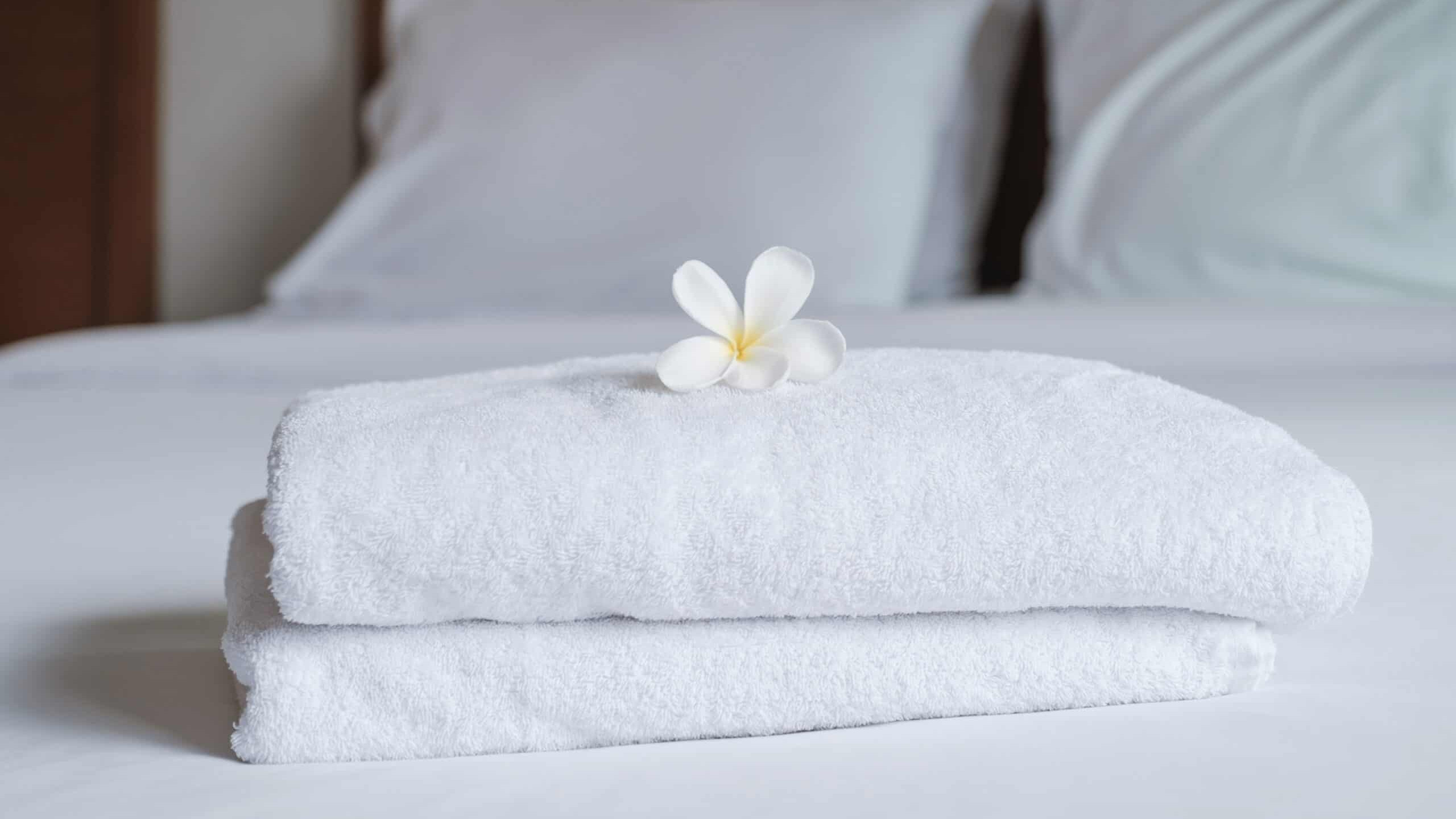 A stack of white towels on a bed with a flower in the middle.