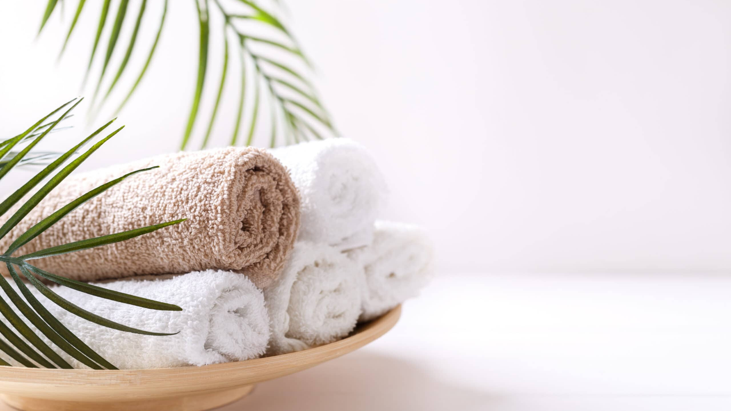 A wooden bowl filled with towels and a palm leaf.